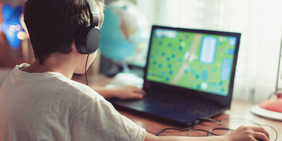 Little dependent gamer kid playing on laptop at home